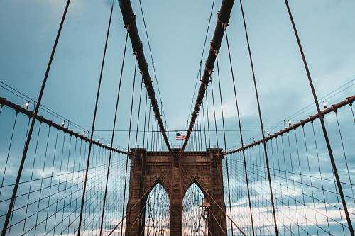 new york low angle photo of brown concrete suspension bridge under blue sky at daytime bridge